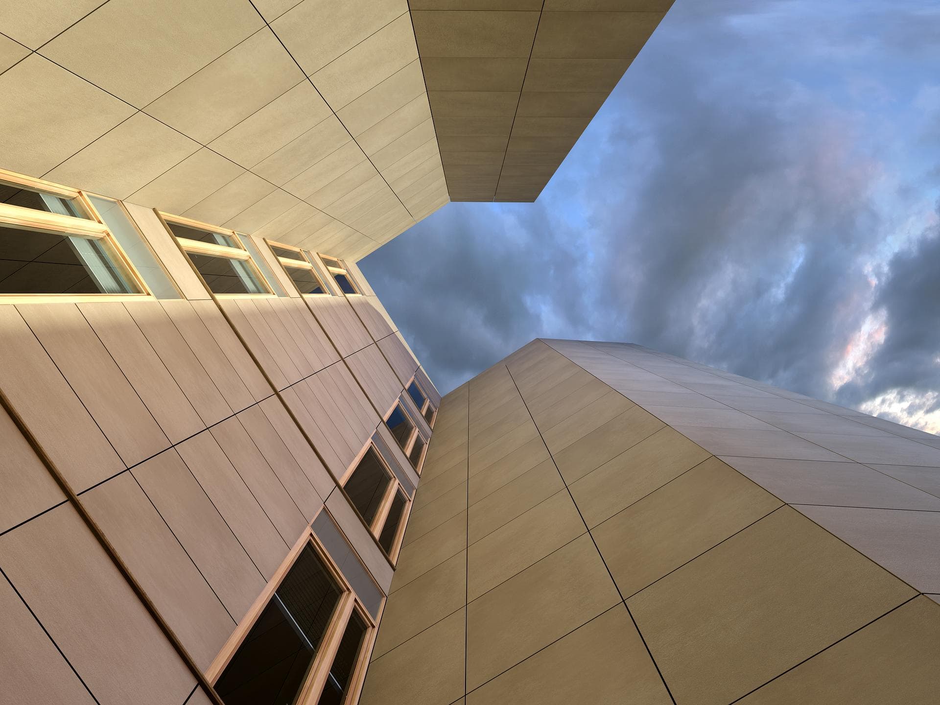 Exterior building facade in almond porcelain Building facade seen from below clad in large matt almond slabs, with windows and a cloudy sky