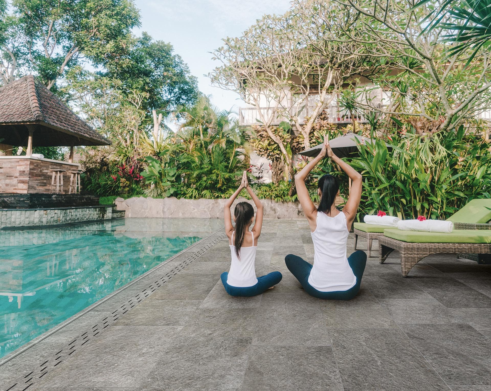Outdoor poolside in grey quartzite-effect stoneware Outdoor poolside paved with grey quartzite-effect stoneware, two people seated, sun loungers and tropical plants