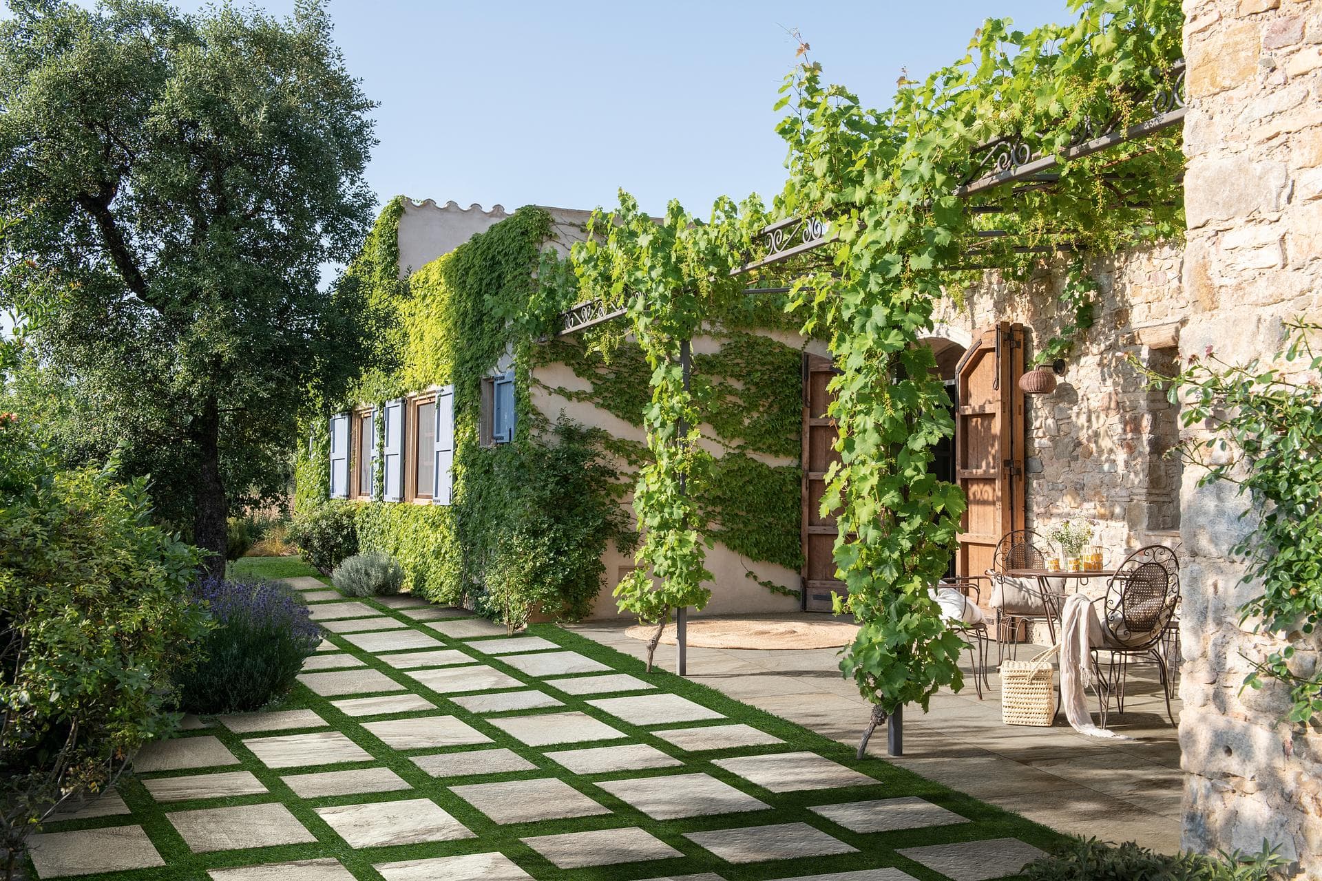 Garden path in stone-effect porcelain slabs Stone house garden with white quartzite-effect slabs laid checkerboard on grass leading to a vine pergola