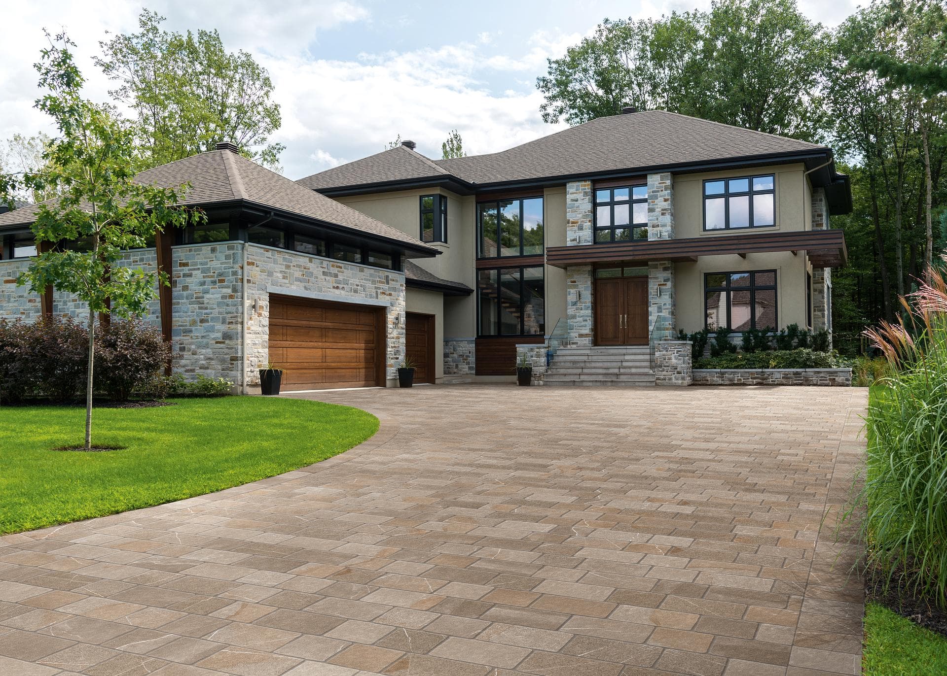 House driveway with stone-effect outdoor paving Driveway of a two-storey house paved with greige stone-effect slabs laid in a running bond beside lawn and shrubs