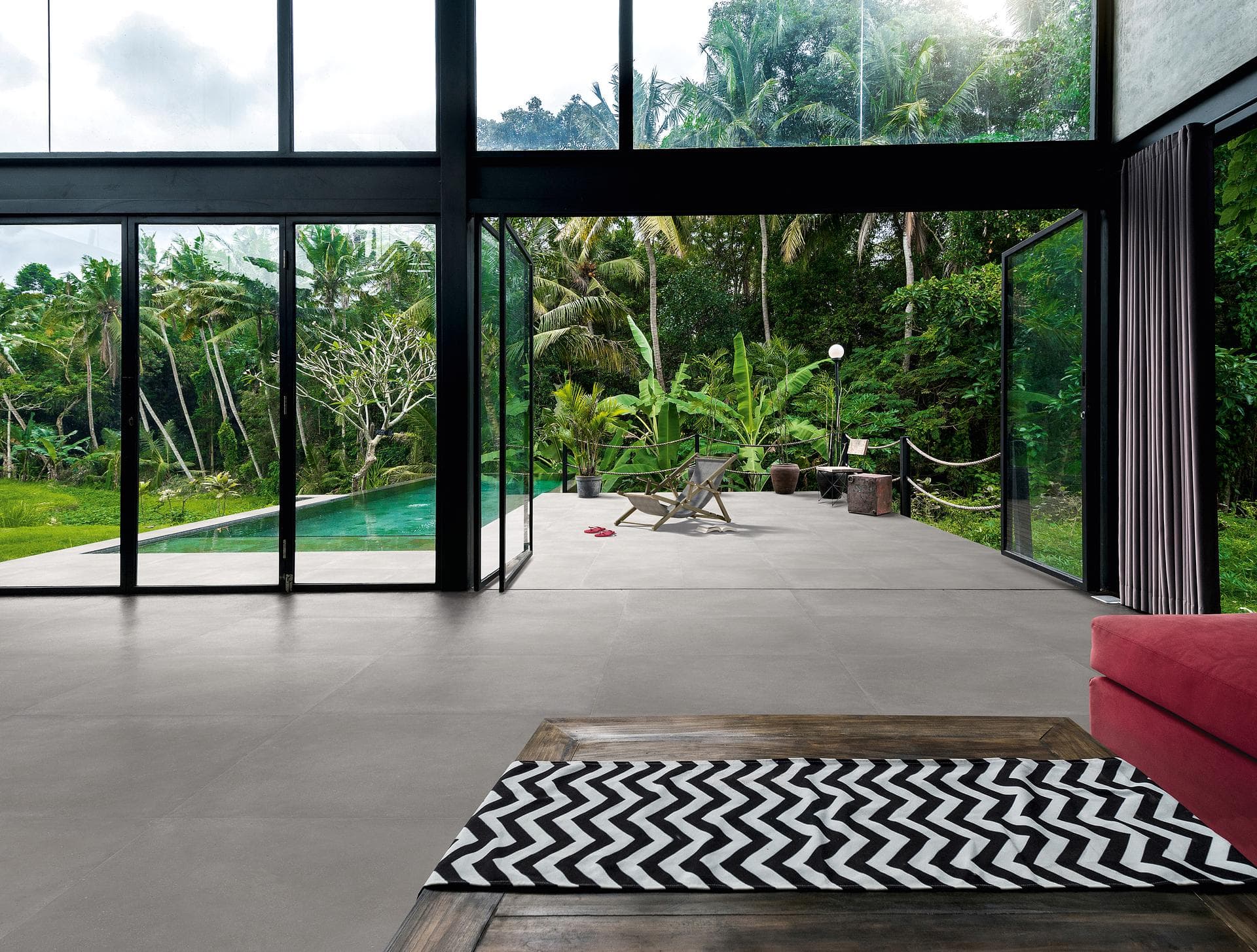 Living room with pool terrace Living room with black glazing opening onto pool terrace, matt grey concrete-effect floor tiles