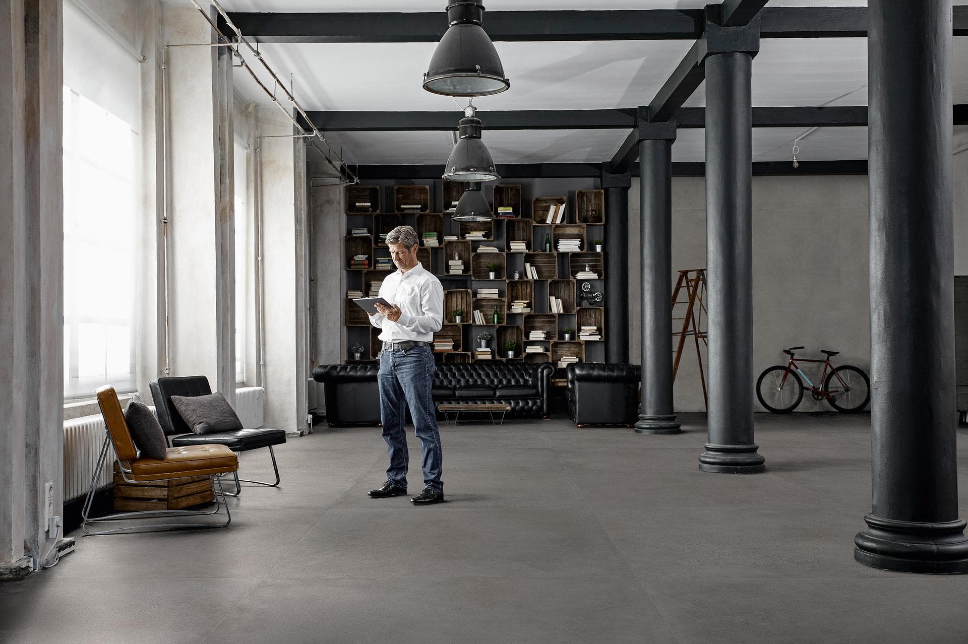 Industrial loft with concrete-effect floor Industrial loft with cast-iron columns, leather sofas and matt dark grey concrete-effect floor tiles